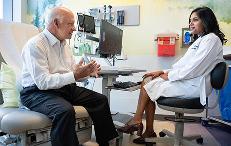 A patient sit in an exam chair, talking to their doctor.