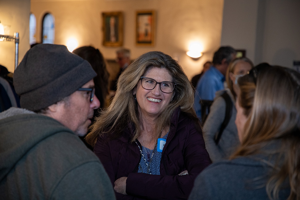 Woman with glasses smiling while talking with other people.